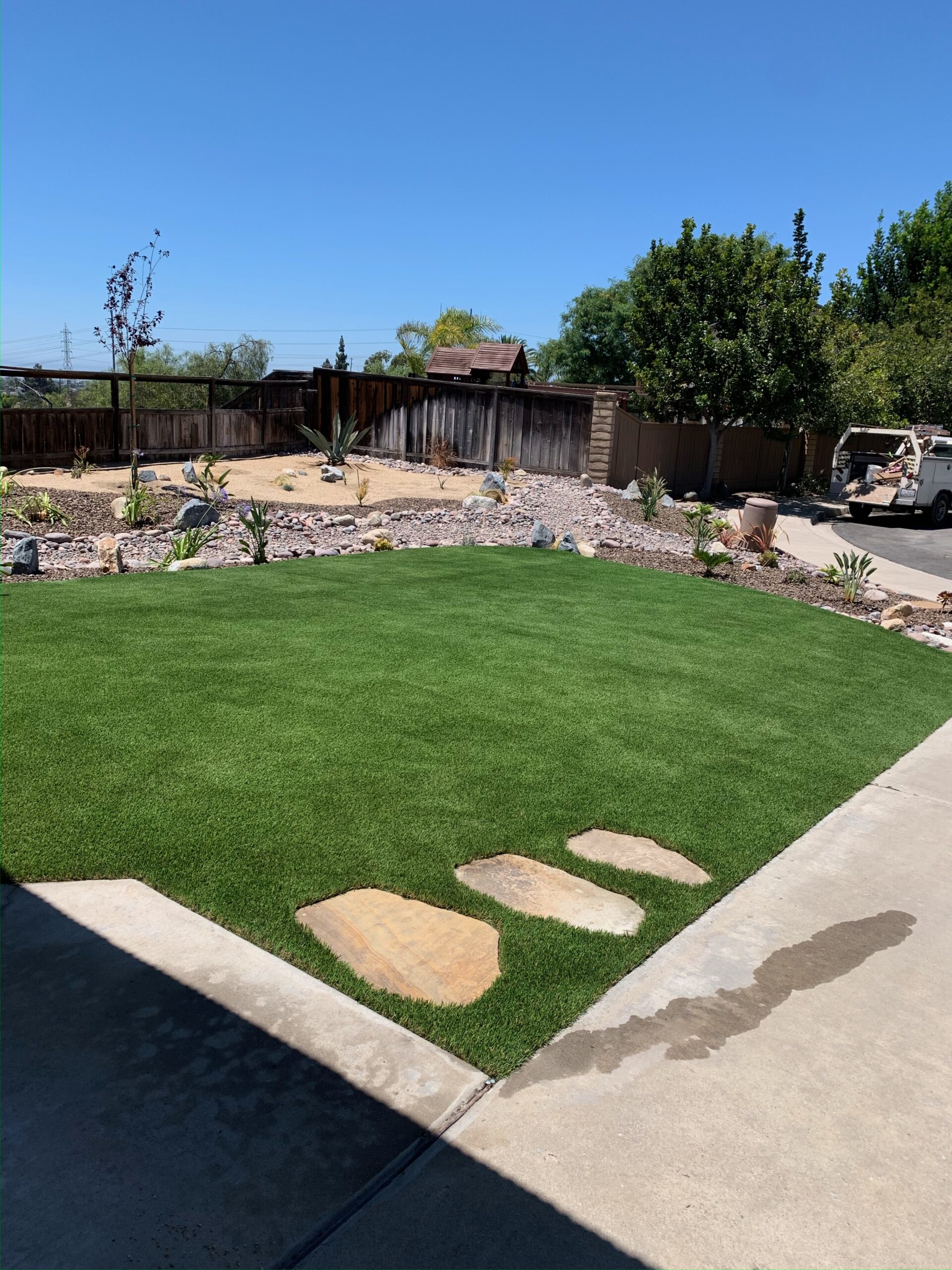 Completed yard project showing turf with natural flagstones, drought-tolerant rock border, and agaves