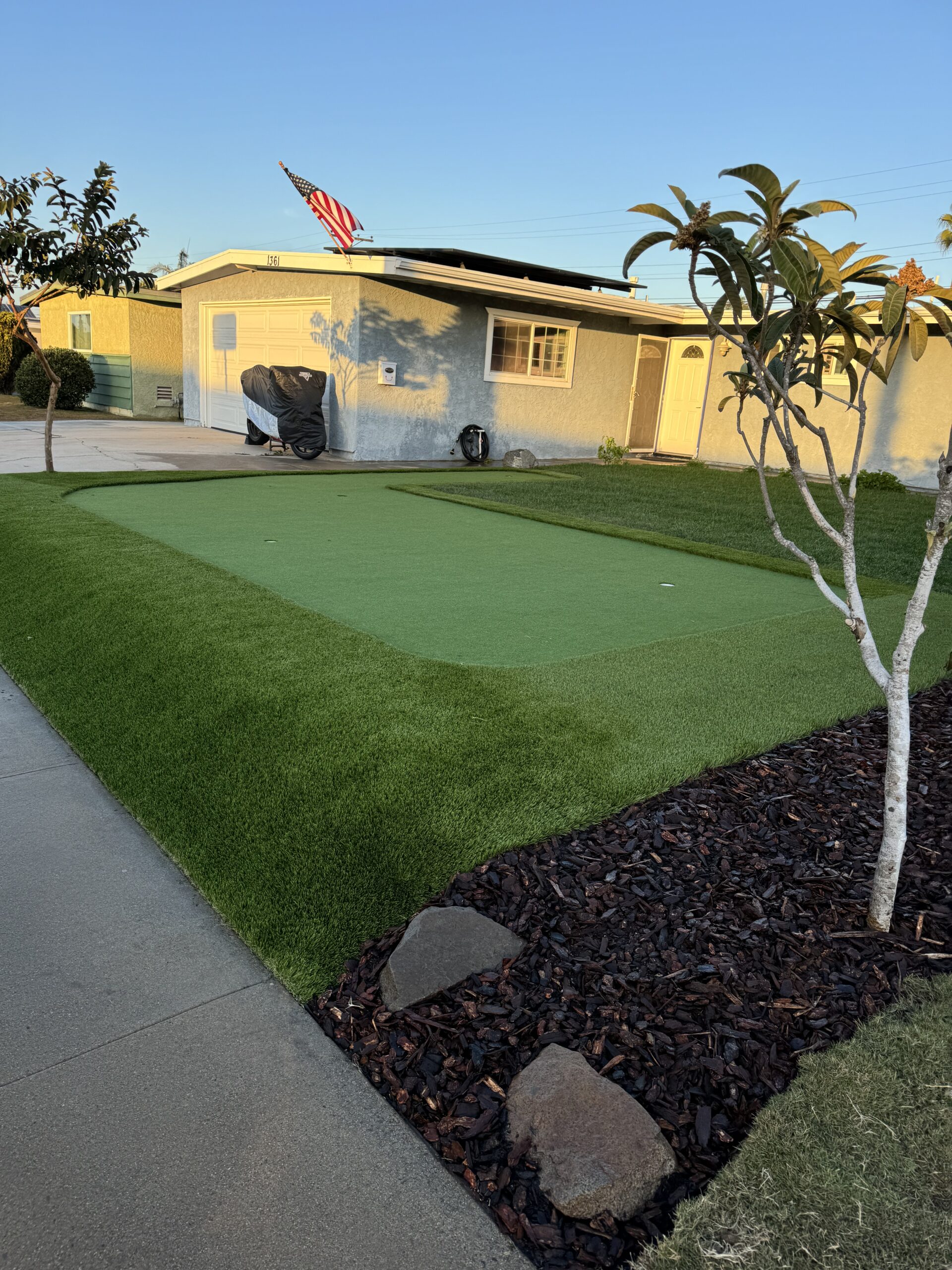 Finished custom front-yard putting green with multiple holes and landscape boulders